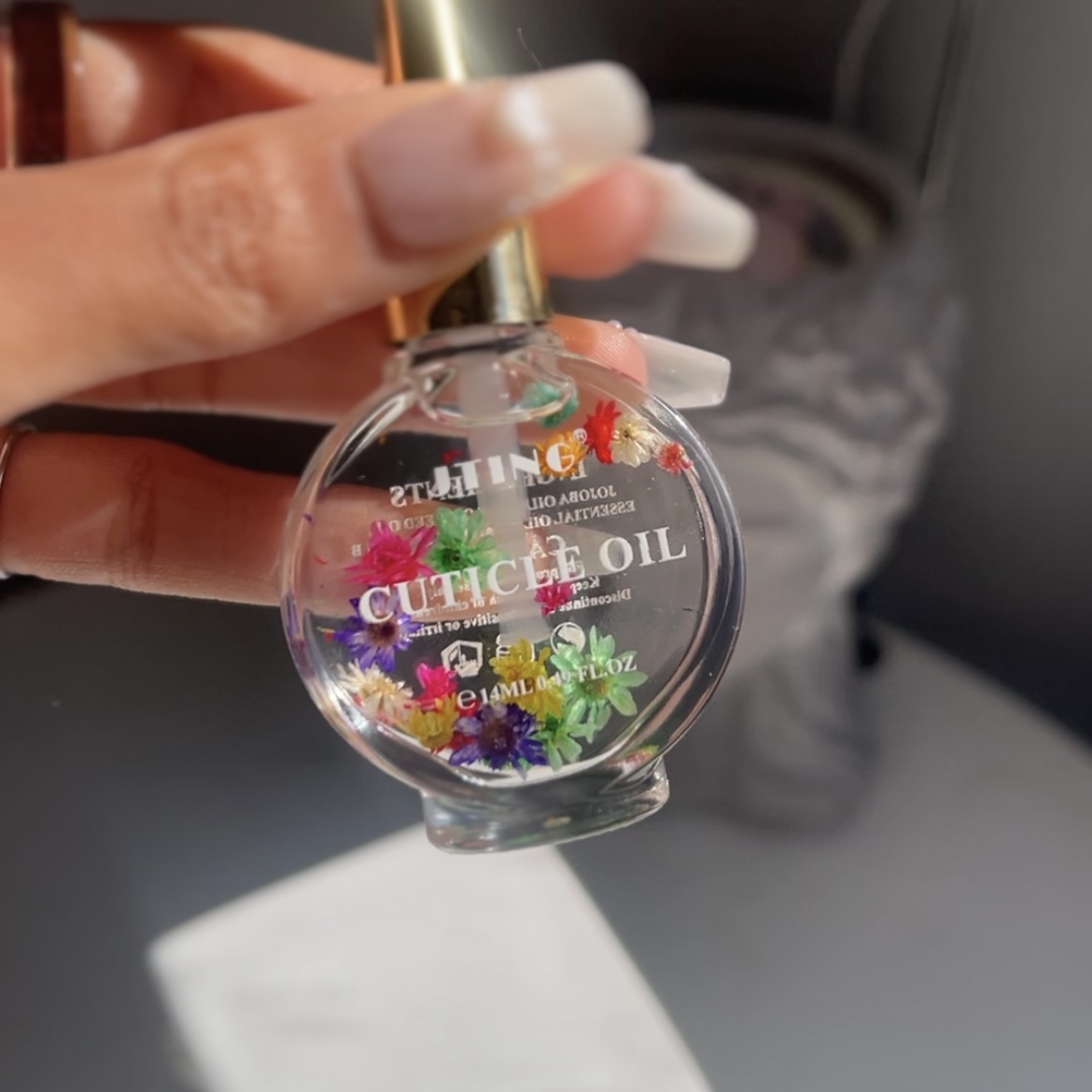 Circular vial of clear oil with colorful flowers floating in the oil