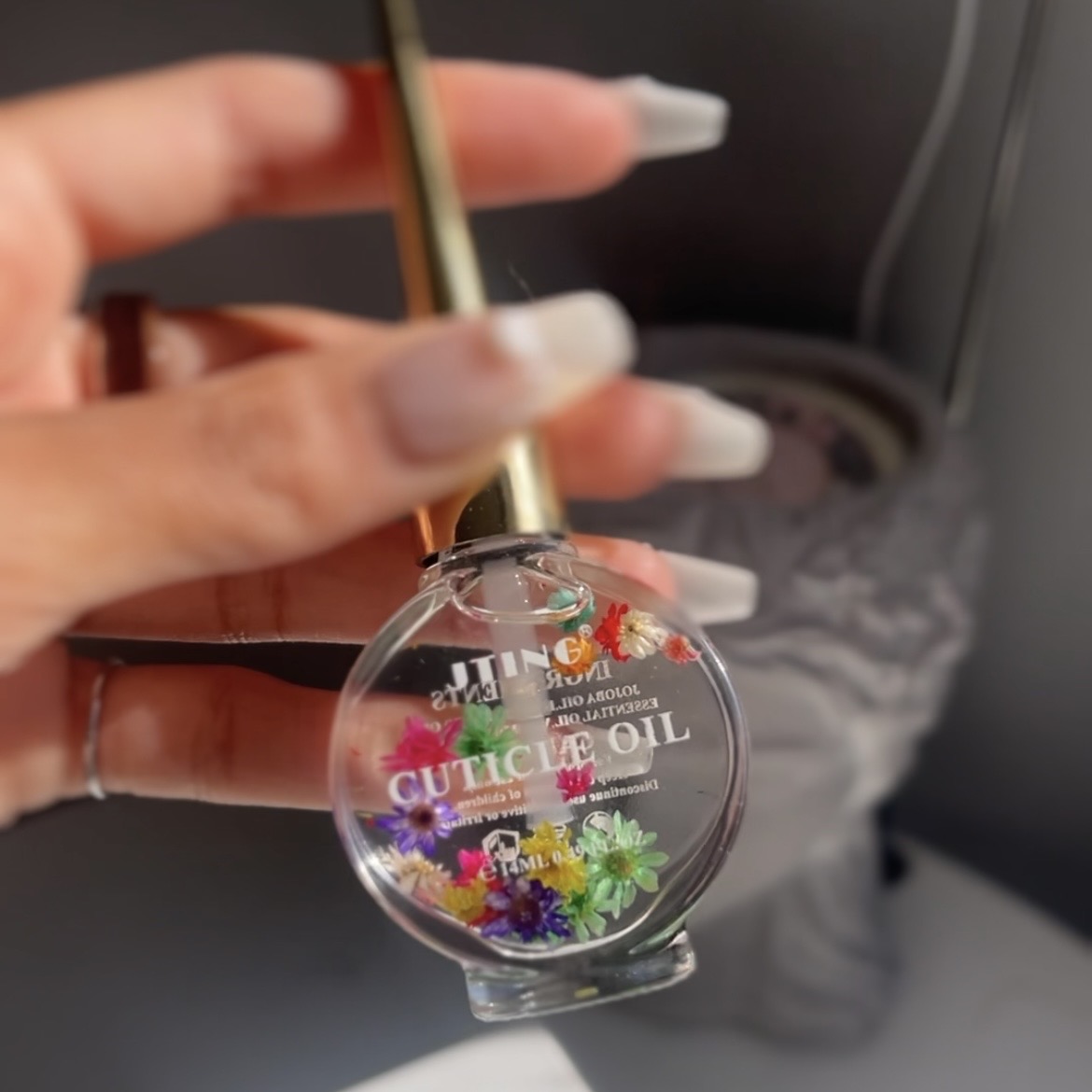 Circular vial of clear oil with colorful flowers floating in the oil