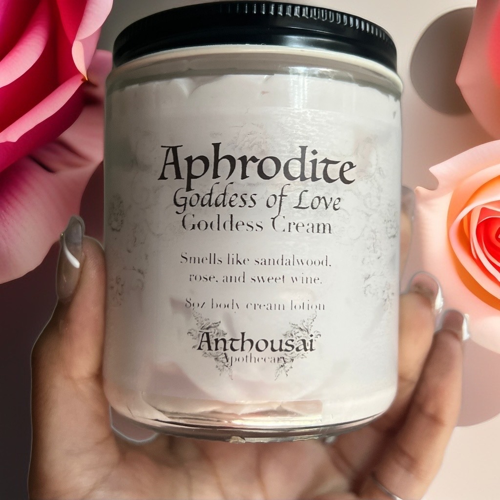 A glass jar filled with a light pink cream lotion and labeled with the text "Aphrodite, Goddess of Love Goddess Cream"